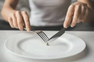 Boulimie_Mains_qui_coupent_un_petit_pois_sur_assiette_vide