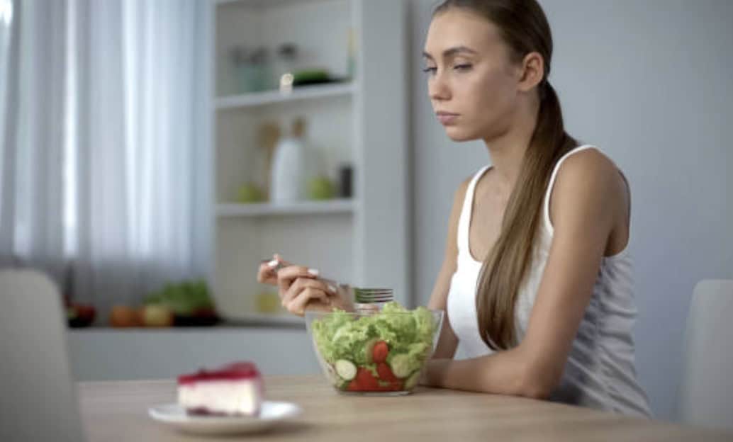 femme qui fait de l'anorexie boulimie mange une salade devant un gâteau