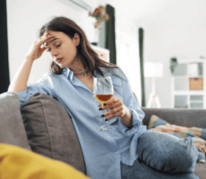 Femme qui boit de l'alcool dans son canapé, la tête dans la main